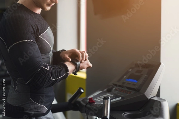 Fototapeta Unrecognizable man using fitness tracker in gym