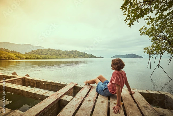 Fototapeta Traveling girl on the wood pier. Pretty young woman and tropical landscape. Summer lifestyle and adventure photo. Fish eye lens image