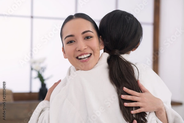 Fototapeta Sincere emotions. Cheerful happy woman hugging her friend while looking at you