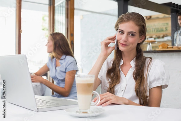 Fototapeta Smiling woman using mobile phone in coffee shop