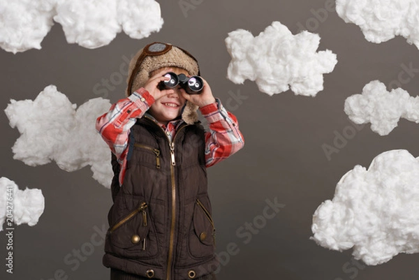 Fototapeta boy dressed as an airplane pilot stands between the clouds and looks through binoculars