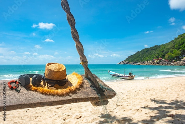 Fototapeta traveling accessory such earphone, music player, hat, sunglass on wooden swing laying under tree on the sea beach, summer time, long weekend, vacation to traveling CONCEPT