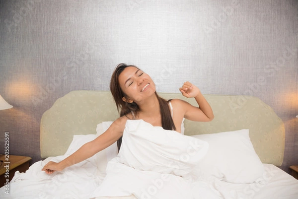 Fototapeta Young beautiful woman waking up in her bed fully rested. Woman stretching in bed after wake up. Healthy lifestyle. Wellness concept