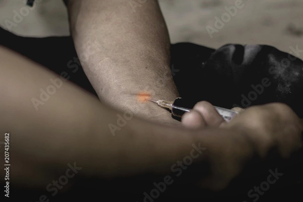 Fototapeta Human hand of a drug addict and a syringe with narcotic syringe sitting on the floor. Anti drug concept.