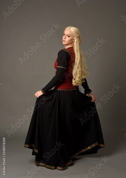 Fototapeta full length portrait of pretty blonde lady wearing  a red and black fantasy medieval gown. standing pose on grey background.