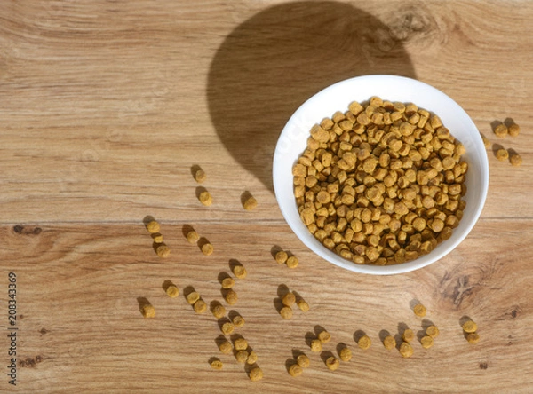 Fototapeta It is the glass full bowl with a dry natural cat food. The granulated pet mix is scattered on a floor.