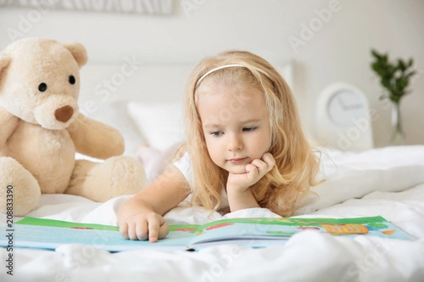 Fototapeta Cute girl reading book on bed at home