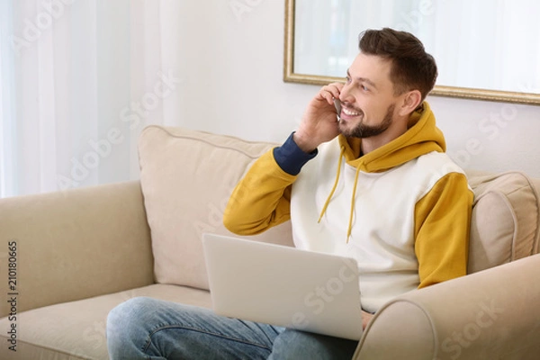 Fototapeta Freelancer talking on phone while using laptop at home