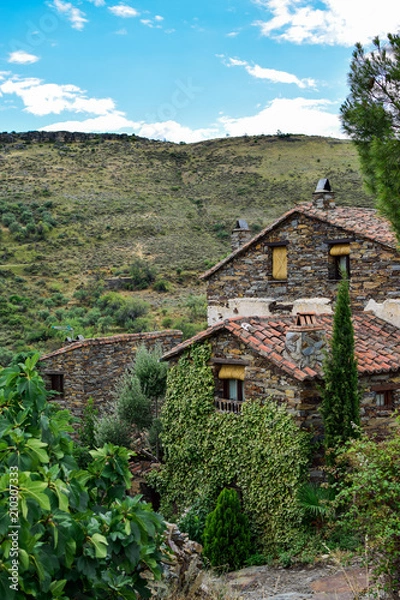 Fototapeta Vertical view of some town houses and their beautiful facades along with a valley in the background ideal for relaxing among nature. Photograph taken in Patones de Arriba, Madrid, Spain