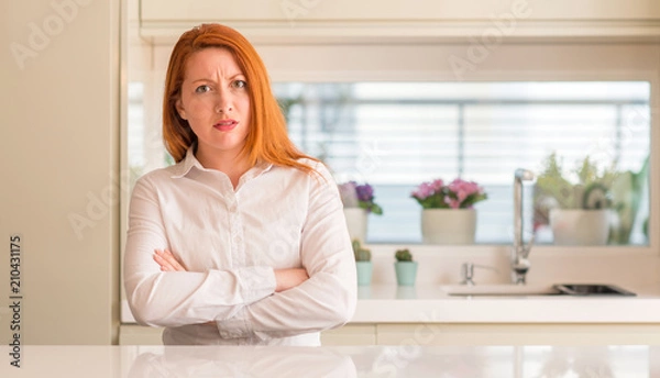 Fototapeta Redhead woman at kitchen skeptic and nervous, disapproving expression on face with crossed arms. Negative person.