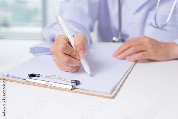 Obraz Close up on asian female doctor hands writing something on clipboard