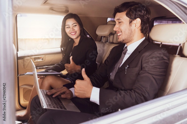 Fototapeta handsome businessman and Business woman sitting and Thumbs up in luxury limousine car, working on laptop computer, Works anytime and anywhere concept.