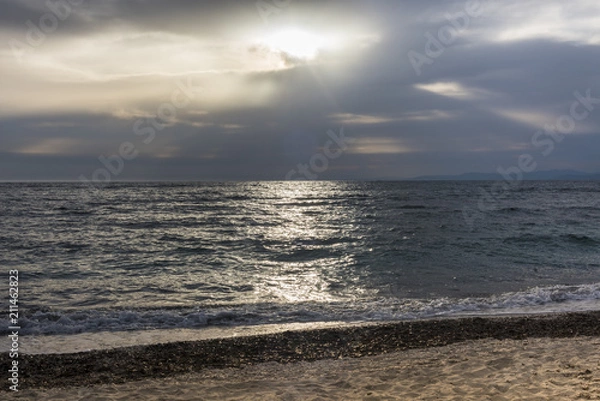 Fototapeta Beach and ocean against sky with dramatic clouds and sun beams, Sardinia, Italy