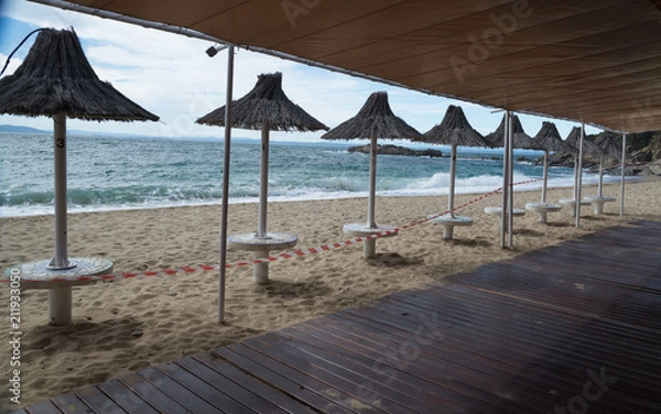 Obraz Sombrillas en una playa de la Costa Brava con mar revuelto y cielo nuboso en invierno