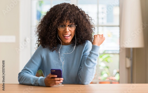 Fototapeta Beautiful african american woman using smartphone screaming proud and celebrating victory and success very excited, cheering emotion