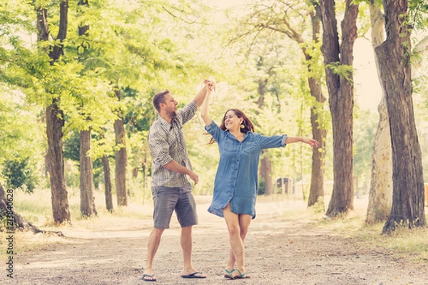 Fototapeta young pretty couple dancing in a green park