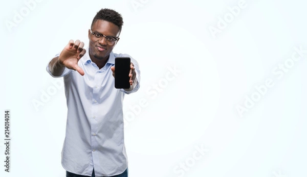 Fototapeta Young african american man using smartphone with angry face, negative sign showing dislike with thumbs down, rejection concept