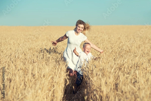 Fototapeta Mom and little son are running around the wheat field.