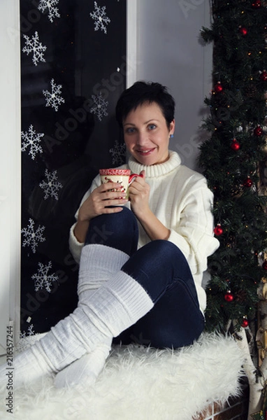 Fototapeta brunette girl in white sweater and white Golf in jeans sitting on a window with snowflakes wood and snowman concept new year in rustic style