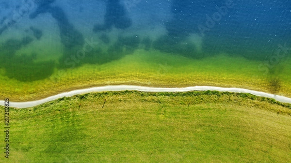 Fototapeta Aerial drone fly. Narrow road along the water and green lawn.