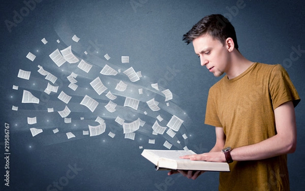 Fototapeta Casual young man holding book with pages flying out of it