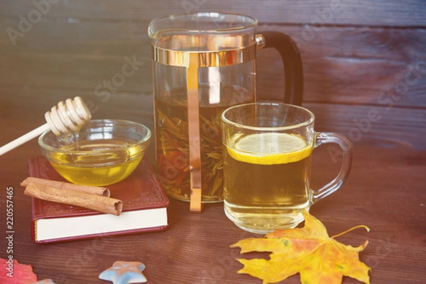 Fototapeta Tea and autumn coziness. A cup of tea, honey, a book, a warm blanket and maple leaves create an autumn mood. Autumn tea on a wooden background. Cosy home