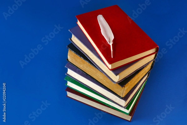 Fototapeta a stack of old books and a feather on a blue background