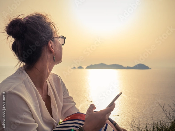 Obraz Young woman using smartphone at sunset in front of the sea on Ponza island coast