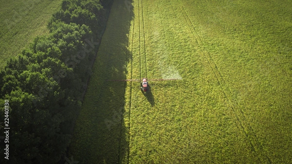 Obraz Aerial shot of tractor on the agricultural field sowing. Red tractors working on the agricultural field with sprayer.