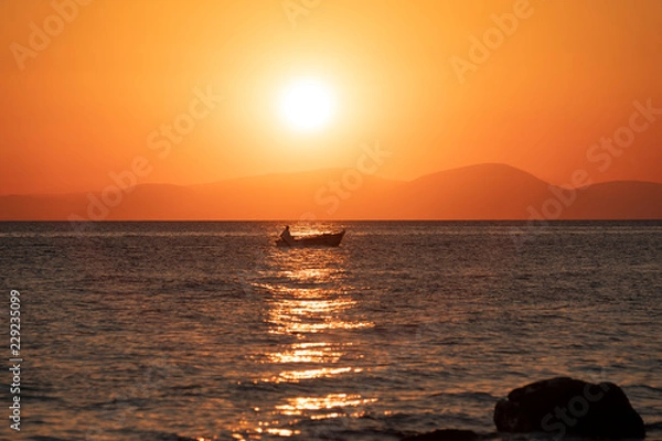 Fototapeta Sonnenuntergang am Meer, Fischerboot fährt der Küste entlang