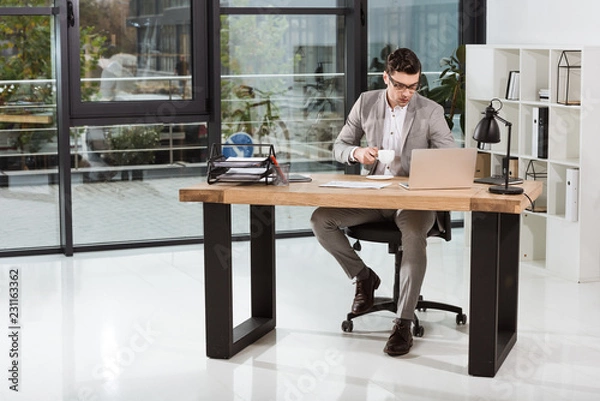 Fototapeta handsome businessman with cup of coffee working with laptop at office