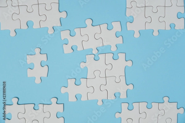 Fototapeta Fragment of a folded white jigsaw puzzle and a pile of uncombed puzzle elements against the background of a blue surface.