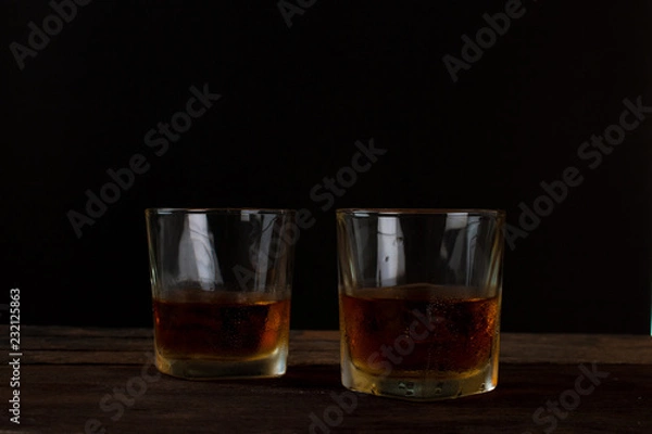 Fototapeta Glass of alcohol scotch whiskey with ice on wooden table and black background