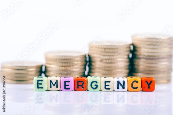 Fototapeta Saving concept, colorful alphabet letter dice text on white reflection desk, spelling EMERGENCY over stacking coins background