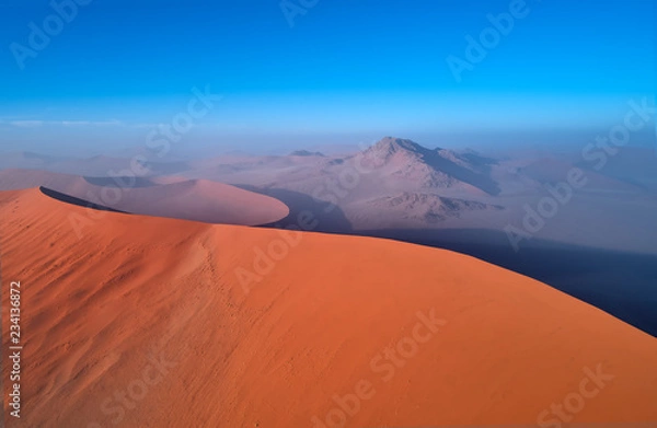 Fototapeta Panoramic, aerial, artistic photo of Namib dunes.  Early morning Namib desert covered in mist. Orange dunes of Namib from above. Desert landscape. Sunrise in Namib-Naukluft  desert. Traveling Namibia.