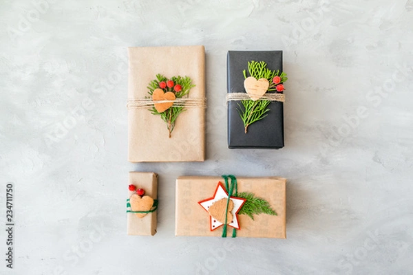 Fototapeta Wrapping Christmas gifts in recycled paper in rustic style. Xmas Gift boxes with craft paper, twine, coniferous branches, red berries and scissors on grey concrete background. Christmas gift pack