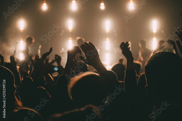 Obraz Crowd of people on a rock concert with the hands raised up close up with silhouettes in a stage backlights 