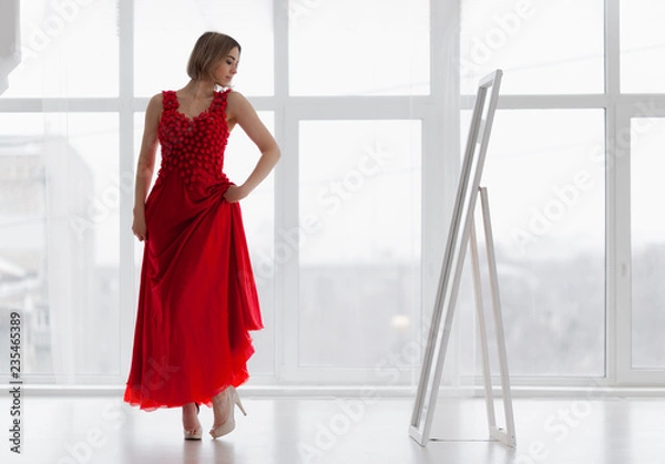 Fototapeta Woman in red dress looks in the mirror