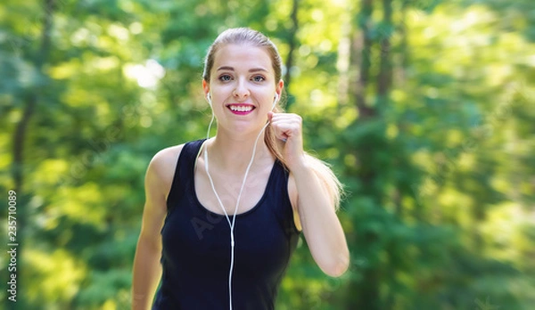 Fototapeta Athletic young woman jogging on a bright summer day in the forest