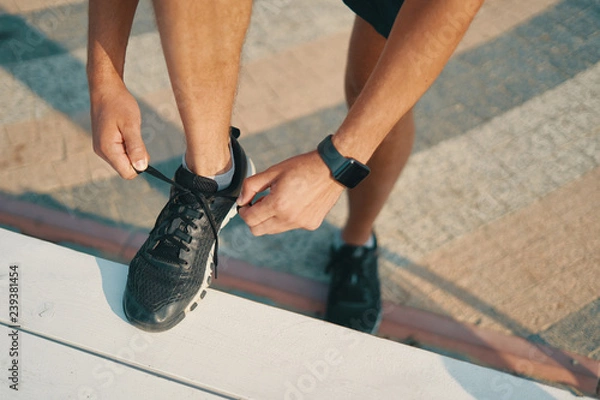 Fototapeta Sportsman ties his black sneakers