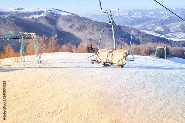 Fototapeta Ski lift with seats going over the mountain