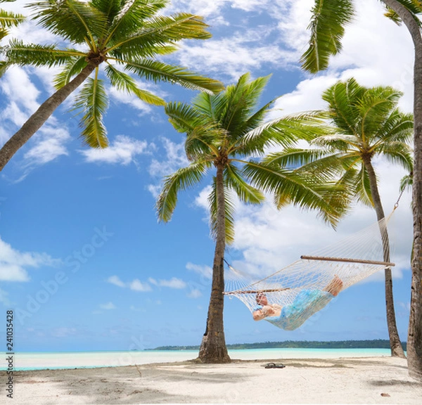 Fototapeta LOW ANGLE: Sleeping woman sways in a rope hammock on tropical white sand beach.