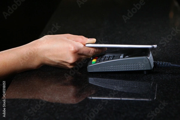 Fototapeta Payment by cell phone. Payment by cell phone through the terminal in the restaurant, shop. Women's hand close-up with cell phone when paying for the purchase.