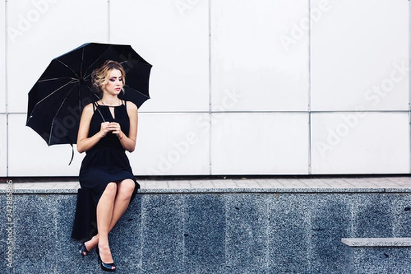 Fototapeta gorgeous woman with an umbrella sits on the parapet and waits.