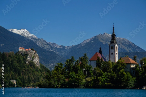 Fototapeta Iconic landscape view of beautiful  St. Marys Church of Assumption on small island,lake Bled in Slovenia .Bled Castle on background. Summer scene travel Slovenia concept. Tourist popular attraction