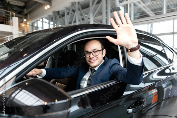 Fototapeta Businessman sitting inside the cabin of a black car welcomes raising his palm up pulling out of the window