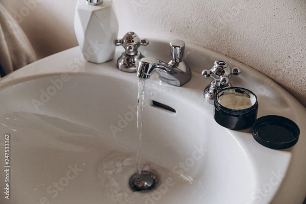 Fototapeta water flows from the tap in the sink, next to the tap there is a bottle of cream and a bottle of soap