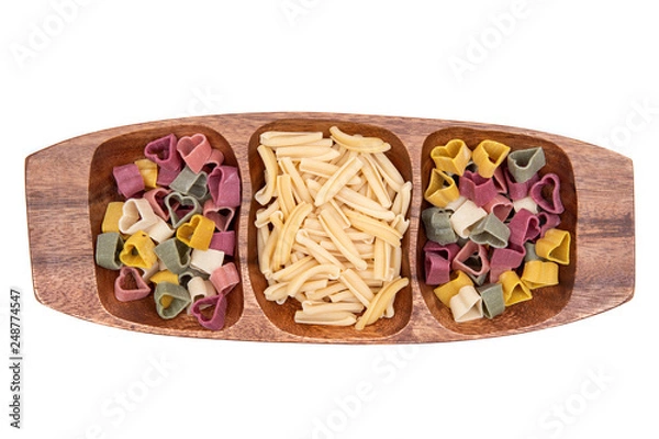 Fototapeta Uncooked Italian Durum wheat semolina heart-shaped and  Casarecce pasta arranged on a long olive wood plate. Isolated on white background.