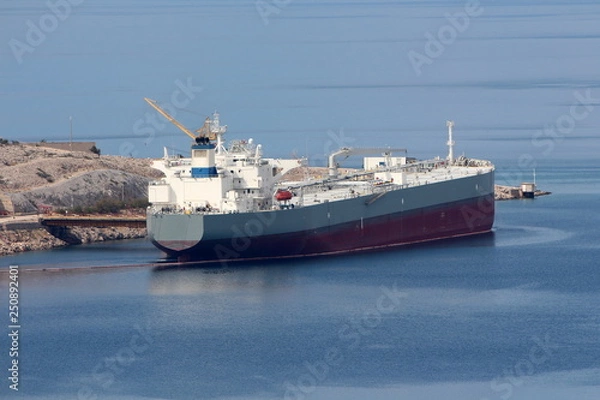 Fototapeta International oil tanker parked in local harbour waiting to be unloaded surrounded with calm dark blue sea and stone shore on warm sunny day