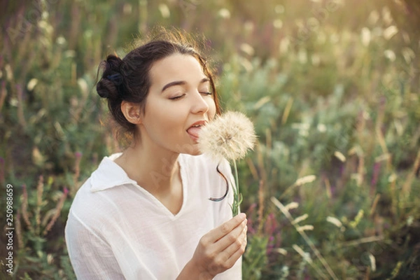 Fototapeta Beautiful young woman with dandelion in a wheat field in the summer sunset. Beauty and summer concept. Touch and feelengs.